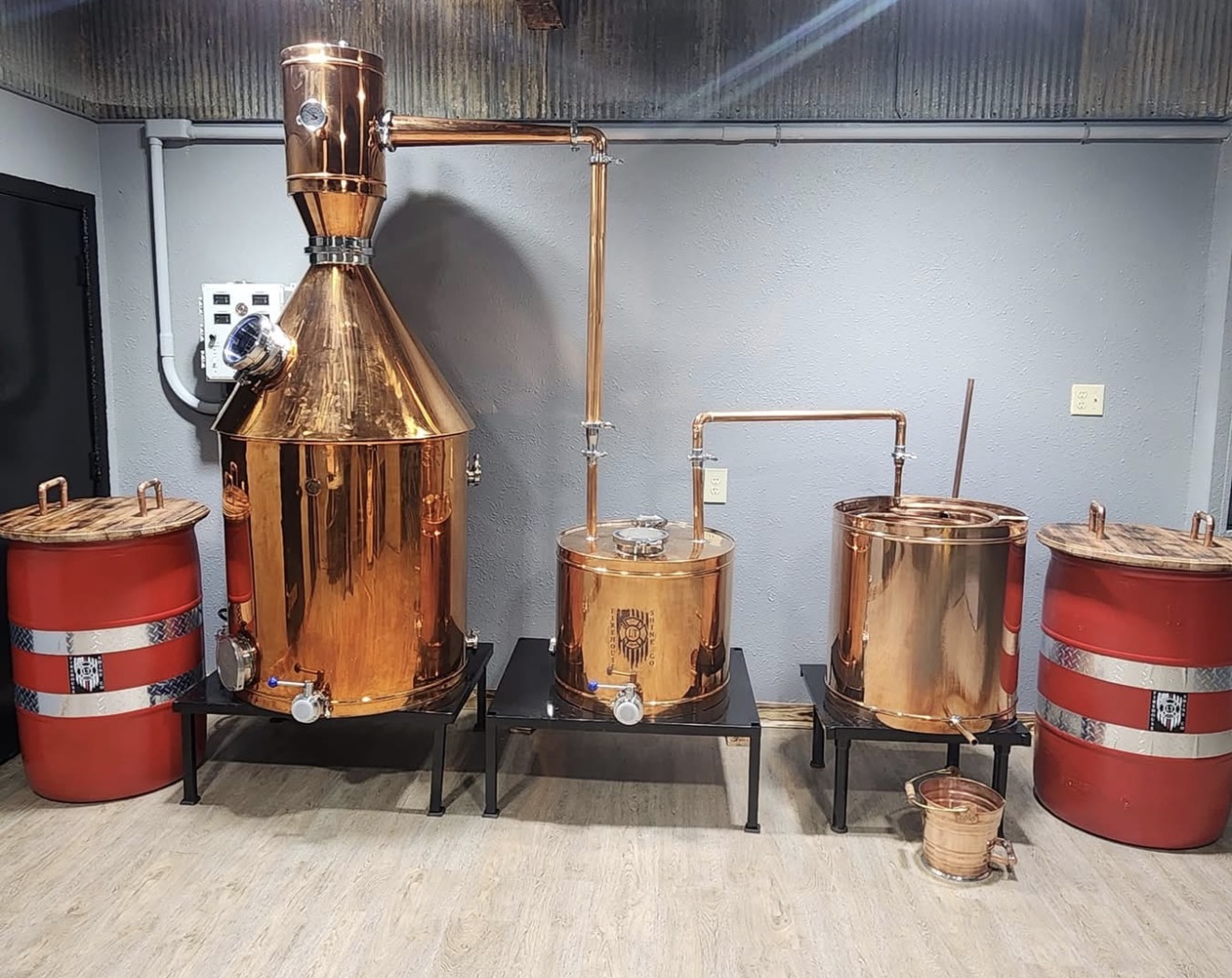 Copper still equipment and red barrels inside Firehouse Shine distillery